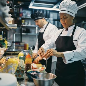 Black female chef cracking an egg while preparing food in a restaurant.