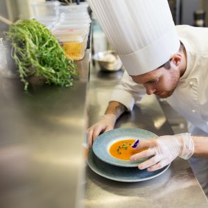 male chef decorating dish with pansy flower